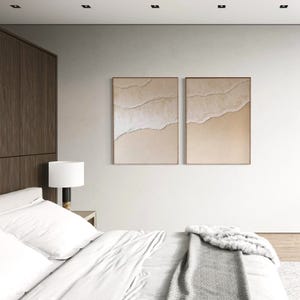 Peut inclure: Deux impressions d'art abstrait avec un fond beige et des lignes blanches, accrochées à un mur blanc au-dessus d'un lit blanc avec une couverture grise.