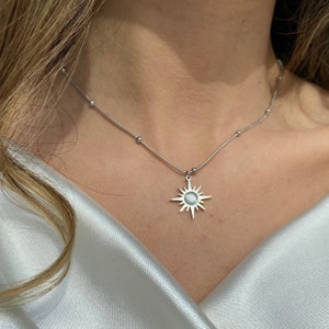 Könnte beinhalten: Eine silberne Halskette mit einem Sonnenanhänger. Die Kette hat eine zarte Kette mit kleinen Perlen.