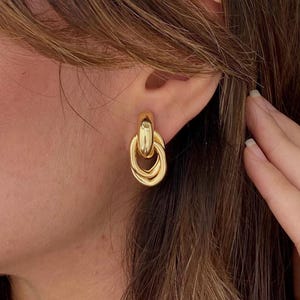 Peut inclure: Boucles d'oreilles dorées de forme ovale avec un design à double boucle. Les boucles d'oreilles ont une finition polie, reflétant la lumière. Ce bijou est un accessoire classique, adapté à diverses occasions.