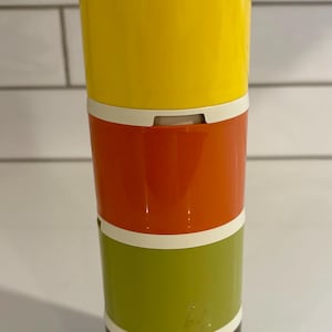 Peut inclure: Ensemble de récipients empilables de style rétro. L'ensemble comprend quatre contenants cylindriques de couleurs jaune, orange, vert et marron, chacun avec un bord blanc. Le récipient supérieur a un couvercle blanc. Les contenants sont empilés verticalement.