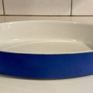 Op de afbeelding: Ovale keramische ovenschaal met een witte binnenkant en een helderblauwe buitenkant. De schaal is leeg en staat op een wit oppervlak. De schaal wordt waarschijnlijk gebruikt om voedsel in te bakken of te serveren.