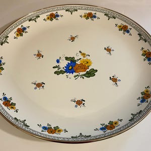 May include: Oval serving platter with a cream-colored background. The platter features a floral design with blue, orange, and yellow flowers. A decorative border with a repeating pattern and gold trim surrounds the edge.
