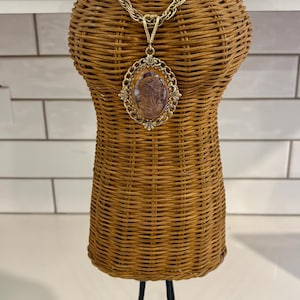 Könnte beinhalten: Eine goldene Kettenkette mit einem Kameenanhänger, der das Profil einer Frau zeigt. Die Kette wird auf einer Weidenbüste mit einem schwarzen Metallständer präsentiert.