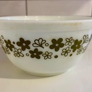 May include: White mixing bowl with a floral pattern in shades of olive green. The bowl has a rounded shape and a simple design, suitable for kitchen use.