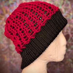 May include: A two-toned beanie featuring a vibrant red upper section with an open, loose-knit lattice pattern and a solid black lower section crafted with a dense, tight-knit stitch. The hat is displayed on a neutral-toned mannequin head.