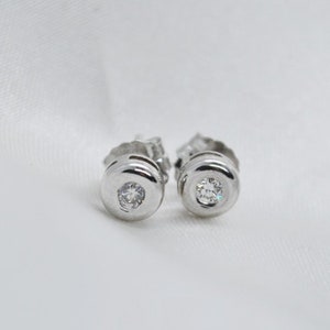 May include: A pair of silver stud earrings with a small, clear diamond in the center of each earring.