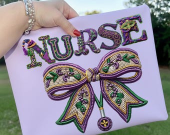 May include: A light purple clutch with the word "NURSE" embroidered in purple, green, and gold. A large bow with similar colors and details is embroidered below the word. The clutch is held by a person.