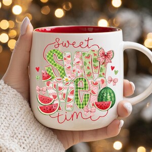 A festive summer coffee mug with a red rim and handle, decorated with watermelon applique graphics