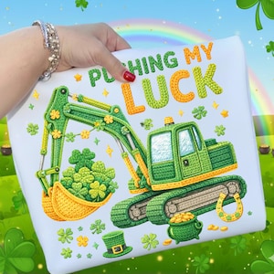 May include: White t-shirt with a St. Patrick's Day theme. The design features a green excavator scooping up shamrocks, with the text "Pushing My Luck" in orange and green. Additional shamrocks and a pot of gold are also included.