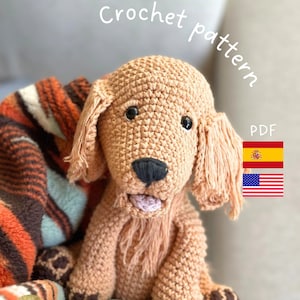 Könnte beinhalten: Ein gehäkeltes Hundespielzeug in Beige mit schwarzen Akzenten, einschließlich Nase und Pfoten. Der Hund hat lange, schlaffe Ohren und sitzt auf einer gestreiften Decke. Der Text "Crochet pattern" befindet sich über dem Hund.