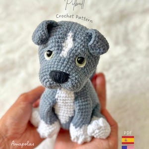Puede incluir: Un juguete de cachorro pitbull tejido a ganchillo en gris y blanco con una mancha blanca en la frente, nariz negra y ojos oscuros. El texto sobre el juguete dice Pitbull Crochet Pattern y abajo a la izquierda Amapolas BABY SHOP.