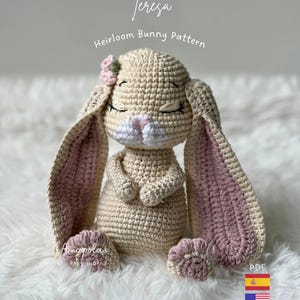 Puede incluir: Un juguete de conejo de ganchillo beige con orejas largas que tienen secciones interiores rosas, ojos cerrados y una pequeña flor rosa en la cabeza. El texto dice Teresa Heirloom Bunny Pattern, Amapolas Baby Shop y PDF con banderas.