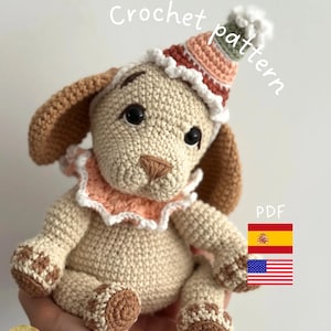 Puede incluir: Muñeco de cachorro tejido a ganchillo con gorro de fiesta. El cachorro es beige con orejas y patas marrones, con un cuello con volantes rosa y blanco. El sombrero está a rayas en tonos rosa, verde y blanco. El texto "Crochet pattern" y "PDF" son visibles.