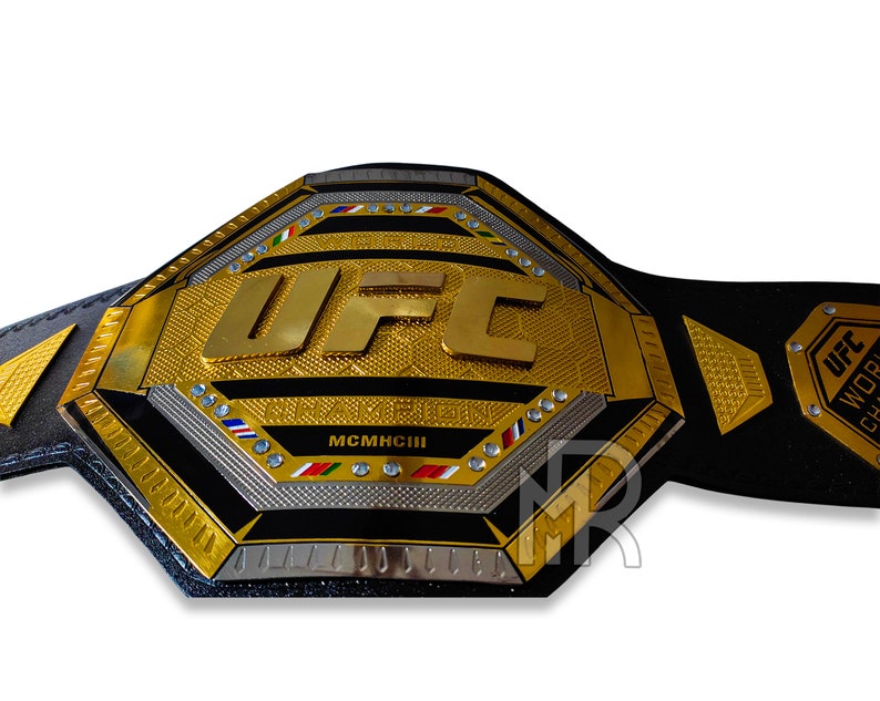 May include: A gold and black UFC World Championship belt with the UFC logo and the year MCMXCIII. The belt is made of leather and has a metal buckle.