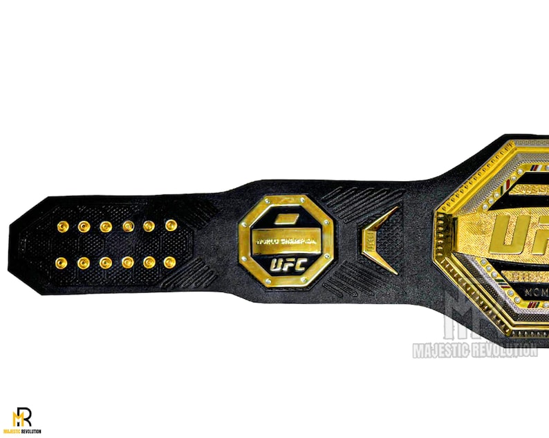 May include: A black leather UFC championship belt with gold accents and the UFC logo. The belt has a hexagonal buckle with the UFC logo and the words "UFC" and "World Championship" inscribed on it.