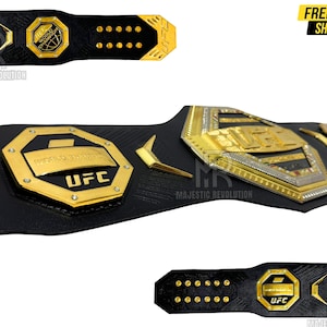 May include: A black leather UFC championship belt with gold accents. The belt features a large octagon-shaped plate with the words "World Champion" and "UFC" in gold lettering. The belt also has smaller plates with the UFC logo and the words "World Champion" in gold lettering.