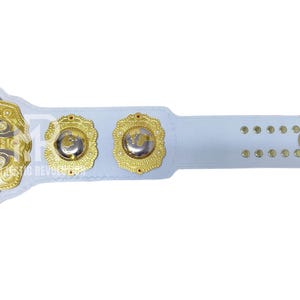 May include: A white and gold championship belt with intricate detailing. The belt features gold medallions and accents, with the words "CONTINENTAL GP CHAMPION" visible. The design includes a white strap with gold edges and rivets.