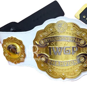 May include: A gold and silver Intercontinental I.W.G.P. Champion wrestling belt with a white strap. The belt features intricate detailing, including the words "Intercontinental I.W.G.P. Champion". The belt has a black backing and a gold buckle.