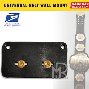May include: Black leather wall mount with two gold-colored metal hooks.  The mount is designed to hold a belt or strap.  "UNIVERSAL BELT WALL MOUNT" is written in yellow letters on a black background at the top of the image.  "SAME DAY DISPATCH" is written in red letters on a white background at the top right of the image.