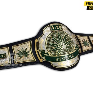Pode incluir: Um cintur&atilde;o de campeonato preto e dourado com um design de folha de maconha verde. O cinto apresenta as palavras "4:20" e "STONER" na frente.