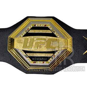 May include: A gold and black UFC championship belt with a large octagonal center plate featuring the UFC logo and the year MCMXCIII. The belt is made of leather and has a black strap.