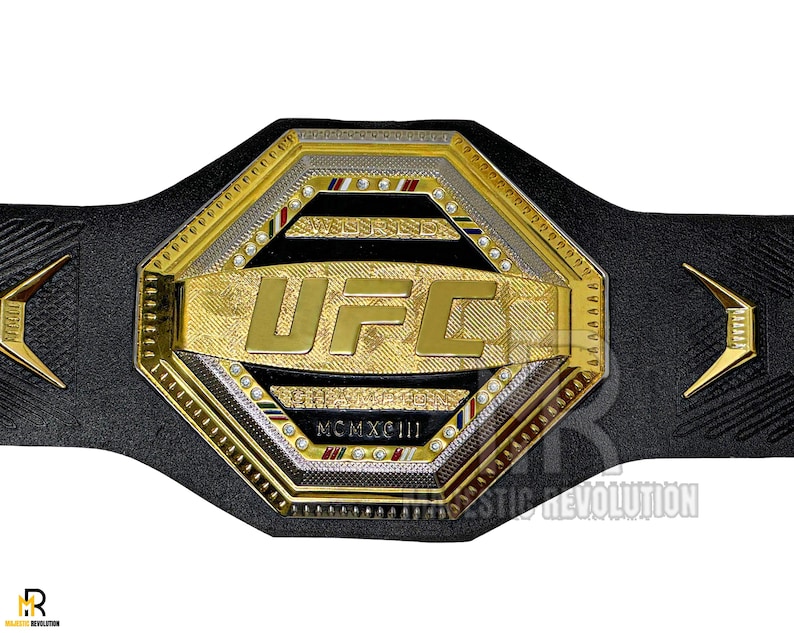 May include: A gold and black UFC championship belt with a large octagonal center plate featuring the UFC logo and the year MCMXCIII. The belt is made of leather and has a black strap.