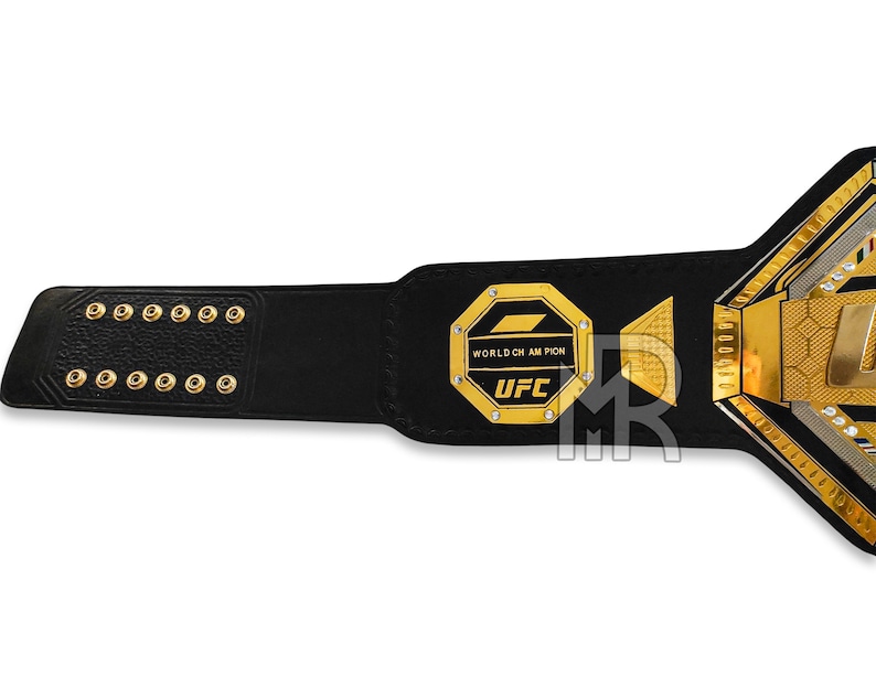 May include: A black leather UFC championship belt with gold accents. The belt features a large octagon-shaped plate with the words "WORLD CHAMPION" and "UFC" in gold lettering.