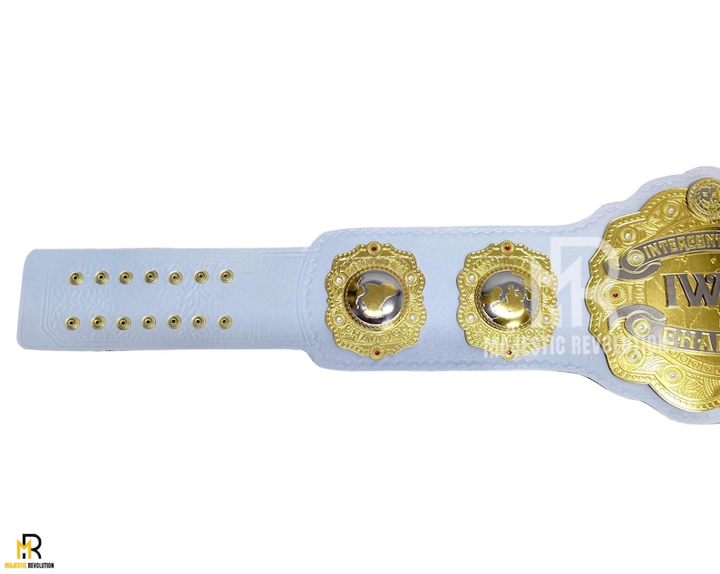 May include: A white wrestling championship belt with gold accents. The belt features a large central plate with the words "Intercontinental IW" and two smaller side plates. The strap has multiple holes for adjustment.