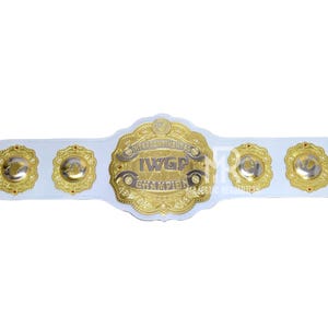 May include: A white wrestling championship belt with gold accents. The belt features a large central gold emblem with the text "IWGP Intercontinental Champion" and four smaller gold emblems.