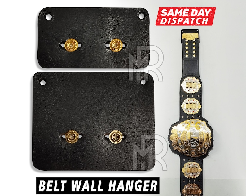 May include: Two black leather belt wall hangers with gold metal hooks. The hangers are designed to hold belts vertically.  BELT WALL HANGER is printed in white letters on the bottom of the image.