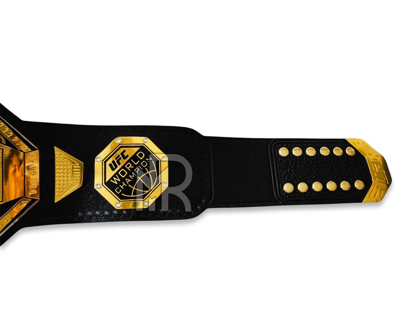 May include: A black leather UFC World Champion belt with a gold buckle and gold accents. The buckle features the UFC logo and the words "World Champion".