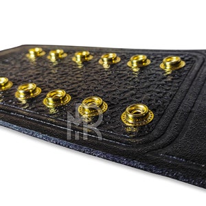 May include: Close-up of a black leather belt with gold metal rivets. The belt has a textured surface and is designed to be worn as a championship belt.