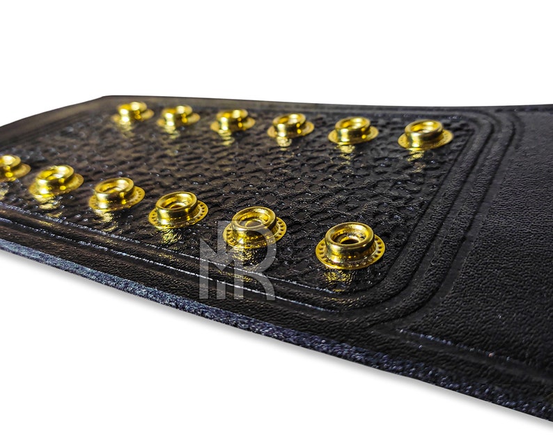 May include: Close-up of a black leather belt with gold metal rivets. The belt has a textured surface and is designed to be worn as a championship belt.