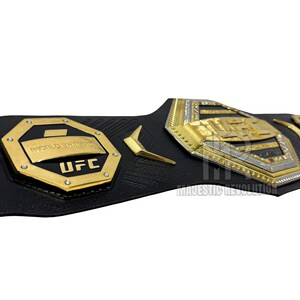 May include: A black leather UFC championship belt with gold and silver accents. The belt features a large octagon-shaped plate with the words "World Champion" and "UFC" in gold lettering.