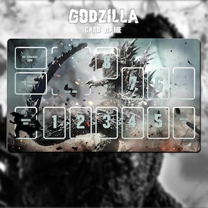 Puede incluir: Tapete de juego de cartas de Godzilla con una ilustración detallada de Godzilla en una escena de batalla. El tapete incluye zonas para estrategia, rabia y mazo de monstruos, con espacios para cartas numerados. El título del juego se muestra en la parte superior.