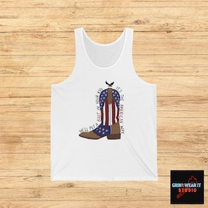Puede incluir: Camiseta sin mangas blanca con un gráfico de una bota de vaquero con el diseño de la bandera estadounidense. El texto en la camiseta dice: "We'll put a boot in your ass, it's the American way."