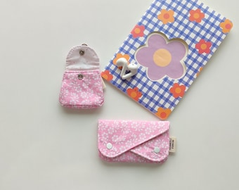 Puede incluir: Dos bolsas de tela rosa con estampados florales blancos. Una bolsa está abierta y la otra está cerrada. Las bolsas están sobre una superficie blanca.