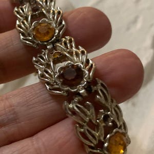 May include: A silver bracelet with a delicate, leafy design and amber-colored rhinestones.