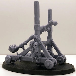 Puede incluir: Una catapulta esquelética gris impresa en 3D con cuatro figuras esqueléticas. La catapulta tiene un mango en forma de cráneo y está decorada con cráneos. Las figuras sostienen armas y cráneos.