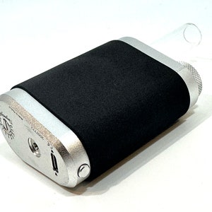 May include: A silver and black electronic cigarette with a black rubber sleeve. The device has a button on the side and a clear glass mouthpiece.
