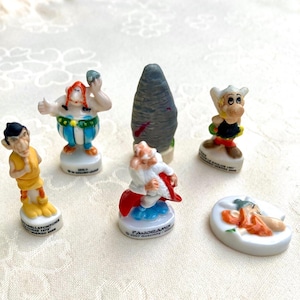 Può includere: Una collezione di piccole e colorate statuette raffiguranti personaggi di una serie a fumetti. Le statuette includono un uomo con i baffi rossi e un abito a righe blu e bianche, e un uomo con barba bianca e mantello rosso.