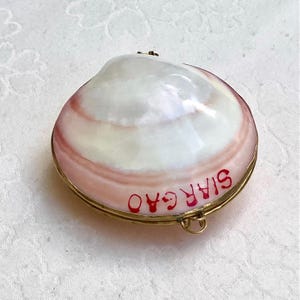 Può includere: Una scatola a cerniera in conchiglia lucida bianca e rosa con bordo e chiusura in metallo color oro. La parola SIARGAO è dipinta a mano in lettere rosse lungo il bordo inferiore della conchiglia. La conchiglia ha una finitura liscia e lucida.