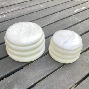 Op de afbeelding: Twee ronde, gestapelde containers gemaakt van een glad, doorschijnend, gebroken wit materiaal met een gemarmerd uiterlijk. Elke container heeft een gelaagd, geribbeld exterieurontwerp met een plat, rond deksel dat vlak op de basis ligt.