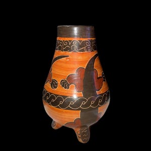 May include: A hand-painted, orange ceramic vase with a dark brown rim and base. The vase features black and brown abstract designs and rests on three small feet. The overall shape is bulbous with a narrow neck.