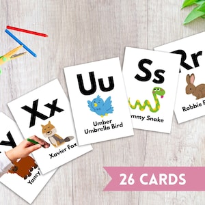 May include: White flashcards with black uppercase and lowercase letters, and colorful illustrations of animals and objects. The cards feature the text "26 CARDS" in a pink banner.