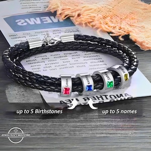 Puede incluir: Un brazalete de cuero negro con cuatro cuentas de plata, cada una con un nombre grabado y una piedra preciosa de color. Los nombres son Leon, Kenny, Janey y Angela. El brazalete tiene el texto "hasta 5 piedras de nacimiento" y "hasta 5 nombres" en la parte inferior.