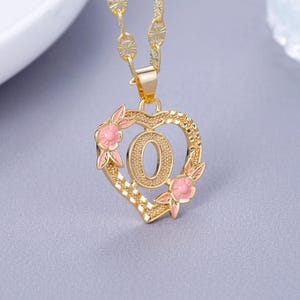May include: Gold heart-shaped pendant necklace with a pink enamel letter O and pink enamel flowers. The chain is a gold curb chain.