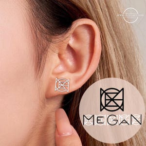 Peut inclure: Gros plan sur une boucle d'oreille argentée avec un motif géométrique. La boucle d'oreille est portée sur une oreille. L'image montre également un logo avec le nom "MEGAN" dans une police stylisée.