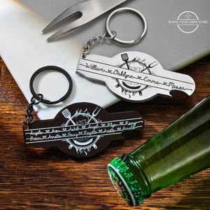 May include: Keychains with a barbecue theme. One keychain is silver with the names William, Oaklynn, Emma, and Mason. The other keychain is black with the names Angela, Arun, Ashil, Angel, Klya, Kaory, Brian, Arnette, Sissy, Rosette, Ariette, and Arnold.