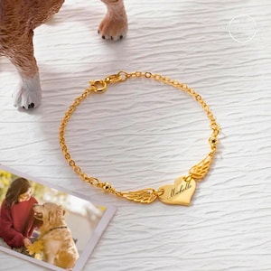 May include: Gold chain bracelet with a heart charm engraved with the name "Michelle" and angel wings.